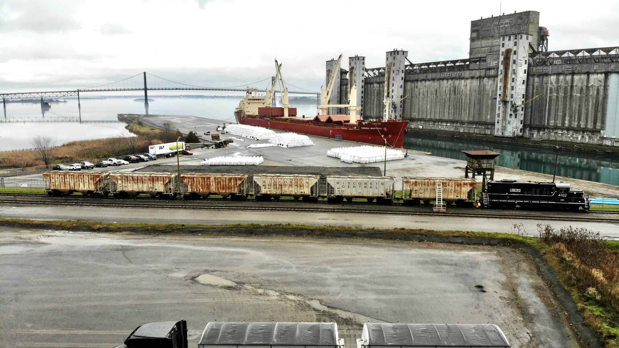 Cargo ship docked beside grain terminal, with railcars and bridge along the waterfront.
